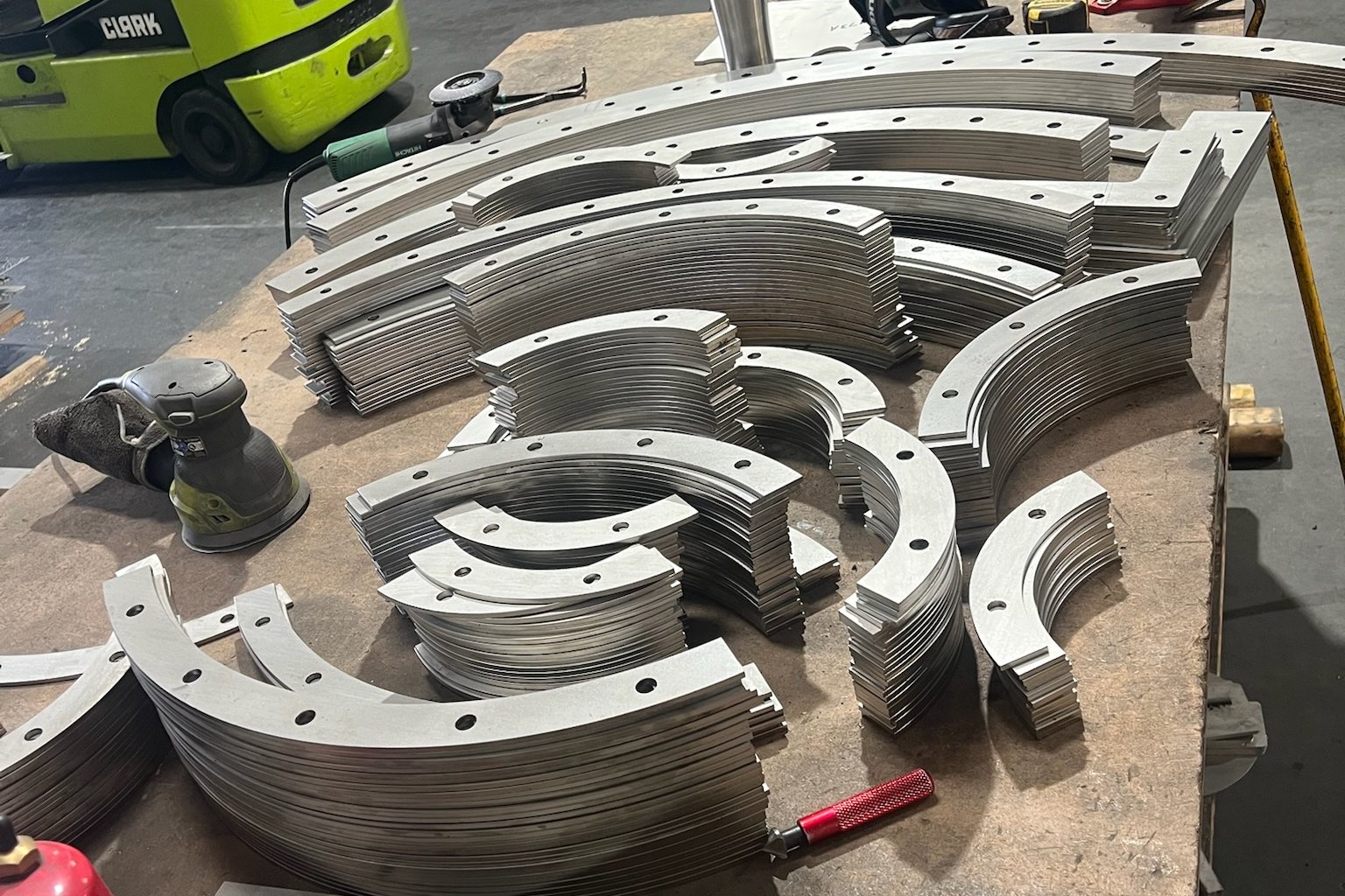 Laser-cut arc segments sorted into matched stacks by radius, bolt holes already cut, on a shop bench.