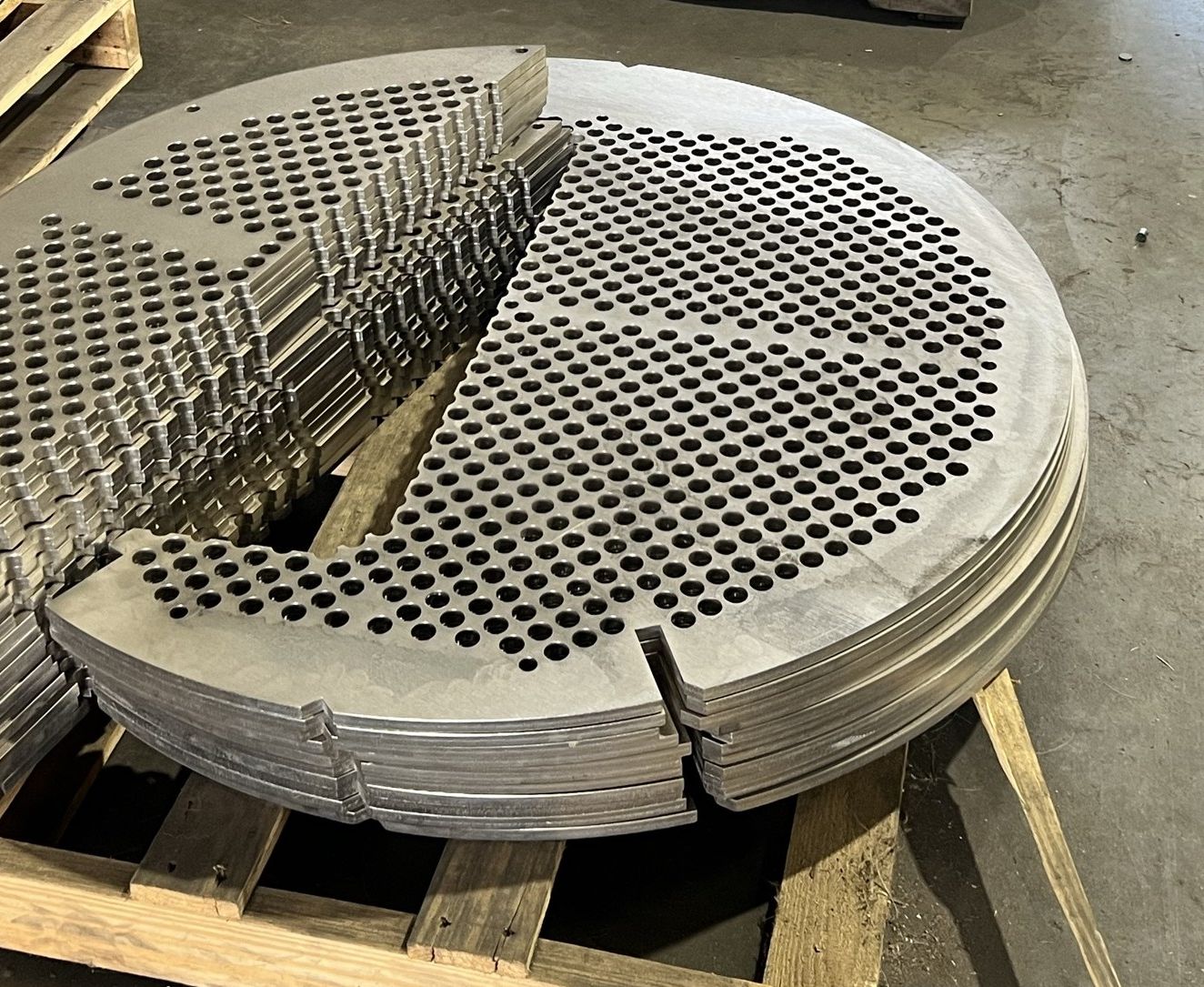 Finished segmental baffles and support plates stacked on a pallet, drilled on triangular pitch with notched edges.