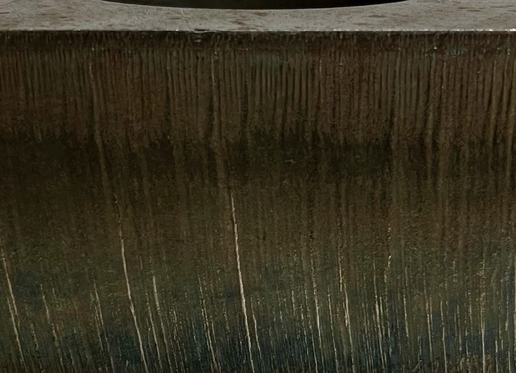 Close-up of a laser-cut face on heavy steel plate showing fine vertical striations and a square top edge.