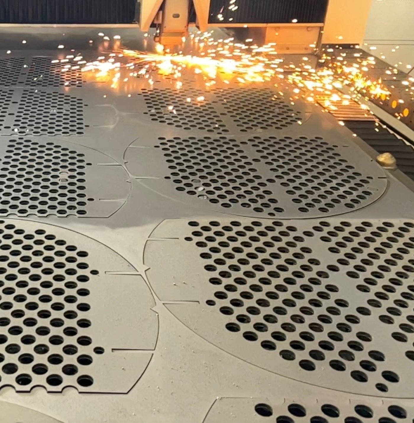 A nest of segmental baffle plates being cut from steel plate, sparks spraying from the cut head.